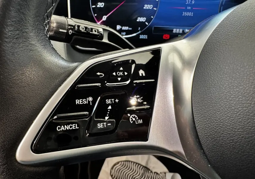 Gros plan sur les commandes du volant à gauche d’un Mercedes GLC 300 E Business Line gris foncé, tableau de bord numérique visible.