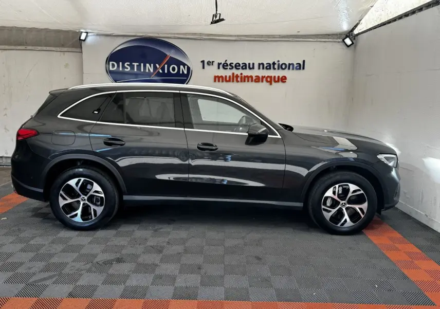 Vue de profil côté gauche d'un Mercedes GLC 300 E Business Line gris foncé, hybride rechargeable, en intérieur showroom.