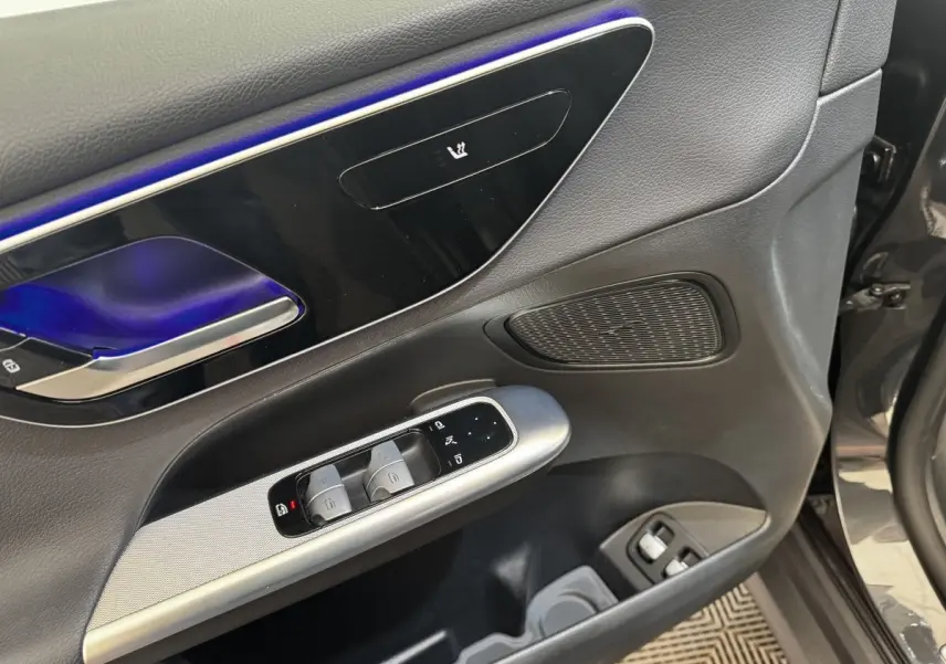 Détail de la porte avant gauche du Mercedes GLC 300 E Business Line 2023 gris foncé, avec commandes de vitres et éclairage d'ambiance bleu.