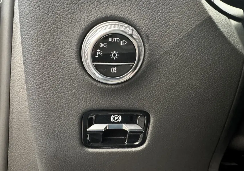 Gros plan sur les commandes d’éclairage et frein à main électrique sur tableau de bord gris foncé du Mercedes GLC 2023.