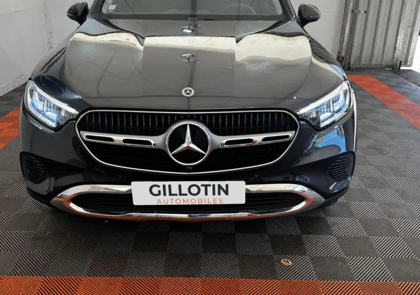 Vue avant rapprochée d’un Mercedes GLC 300 E Business Line 2023 gris foncé avec calandre chromée et phares LED allumés.