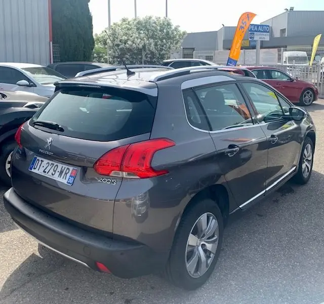 Peugeot 2008 gris métallisé vue 3/4 arrière droit, avec barres de toit et feux arrière distinctifs.