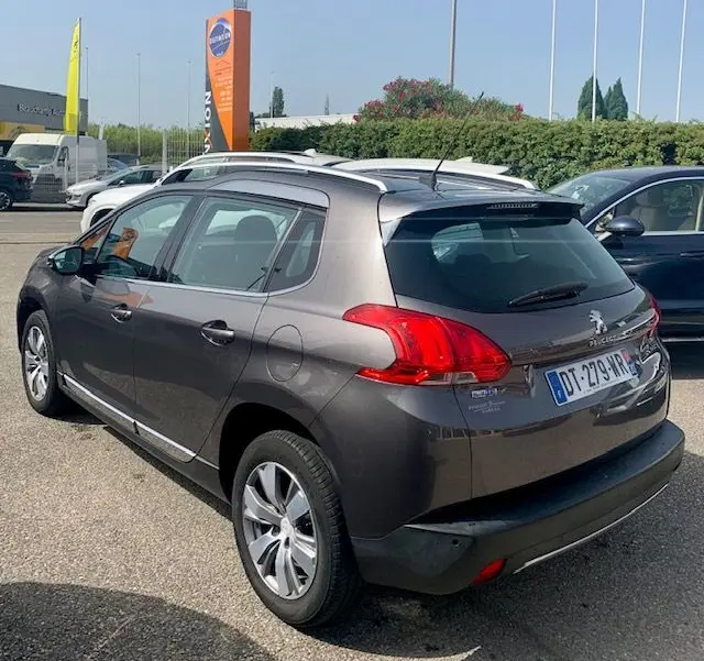 Peugeot 2008 gris métallisé vue en 3/4 arrière droit, avec barres de toit et feux arrière distinctifs.