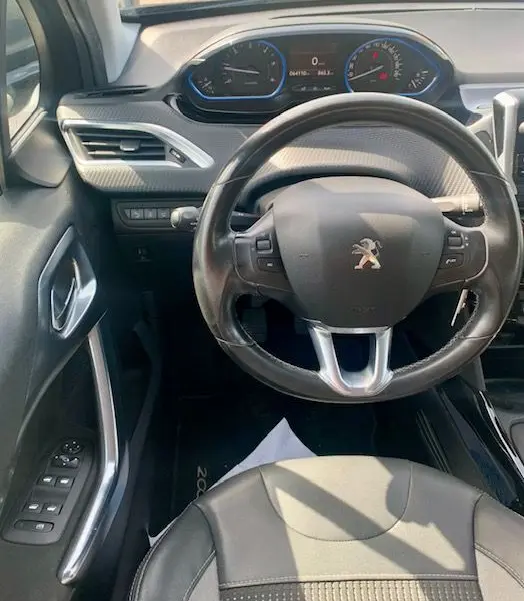 Vue intérieure frontale du tableau de bord et volant Peugeot 2008 gris, avec compteurs numériques et commandes au volant visibles.