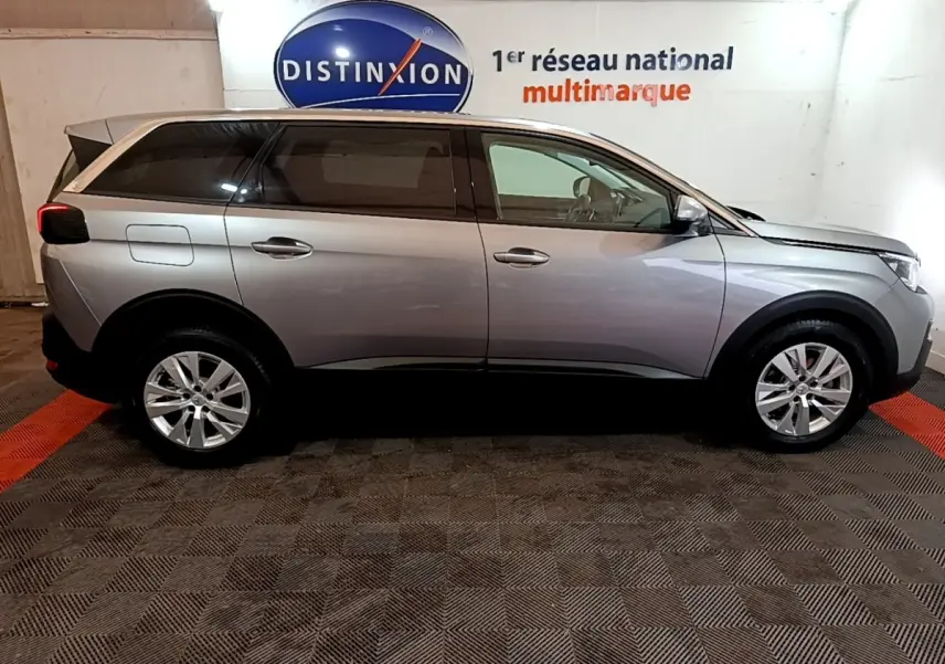 Vue de profil côté gauche d'un Peugeot 5008 gris foncé garé en intérieur avec jantes argentées et vitres teintées.