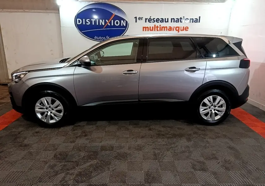 Vue latérale droite d’un Peugeot 5008 gris foncé garé en intérieur avec logo Distinxion en arrière-plan.