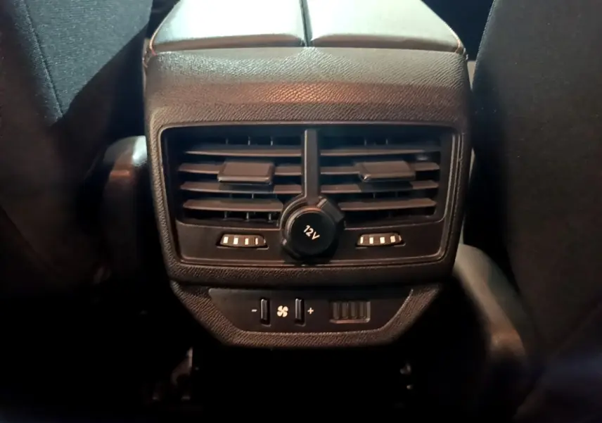Vue rapprochée des commandes de ventilation arrière et prise 12V du Peugeot 5008 gris foncé, entre les sièges avant.
