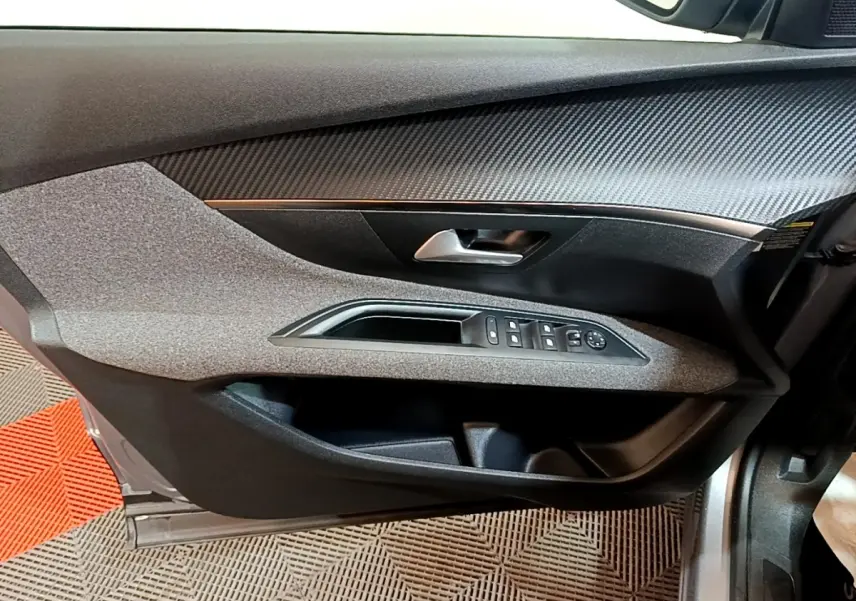 Vue intérieure côté gauche de la porte avant gris foncé du Peugeot 5008 avec commandes électriques des vitres et poignée argentée.