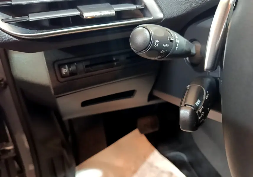 Gros plan sur la commande des phares et régulateur de vitesse côté gauche du tableau de bord d’un Peugeot 5008 gris foncé.