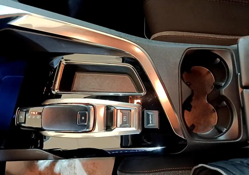 Vue plongeante sur la console centrale noire brillante du Peugeot 5008 gris foncé, avec levier de vitesse et porte-gobelets.