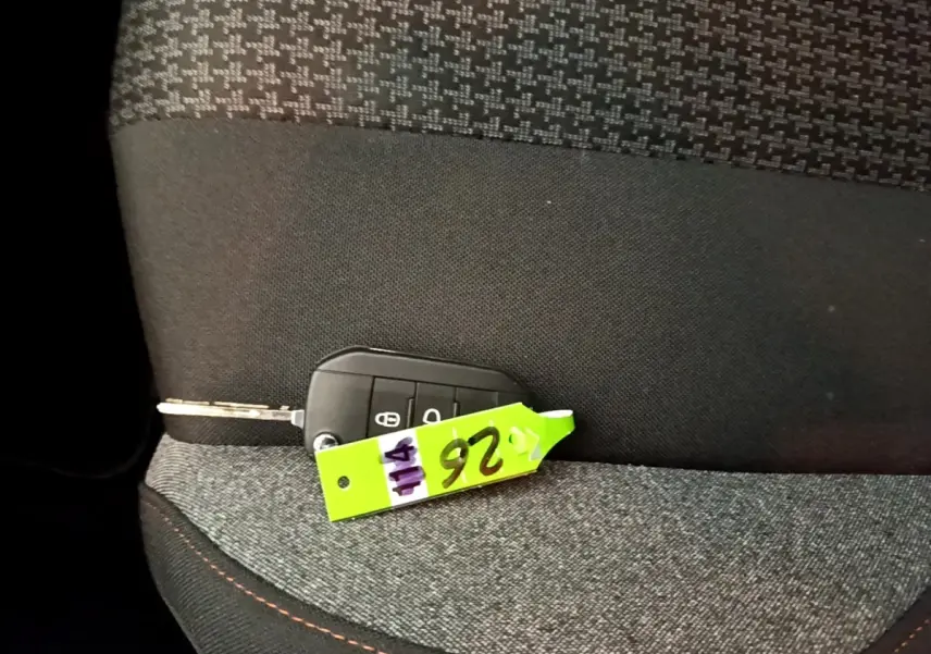 Clé de voiture Peugeot 5008 posée sur un siège tissu gris foncé avec surpiqûres orange, vue intérieure rapprochée.