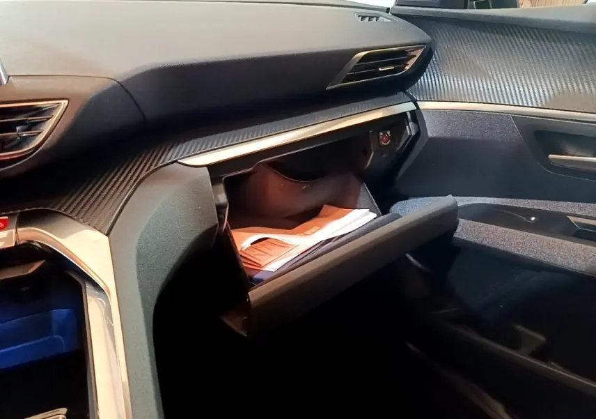 Vue intérieure côté passager du tableau de bord gris foncé du Peugeot 5008 avec boîte à gants ouverte et documents visibles.