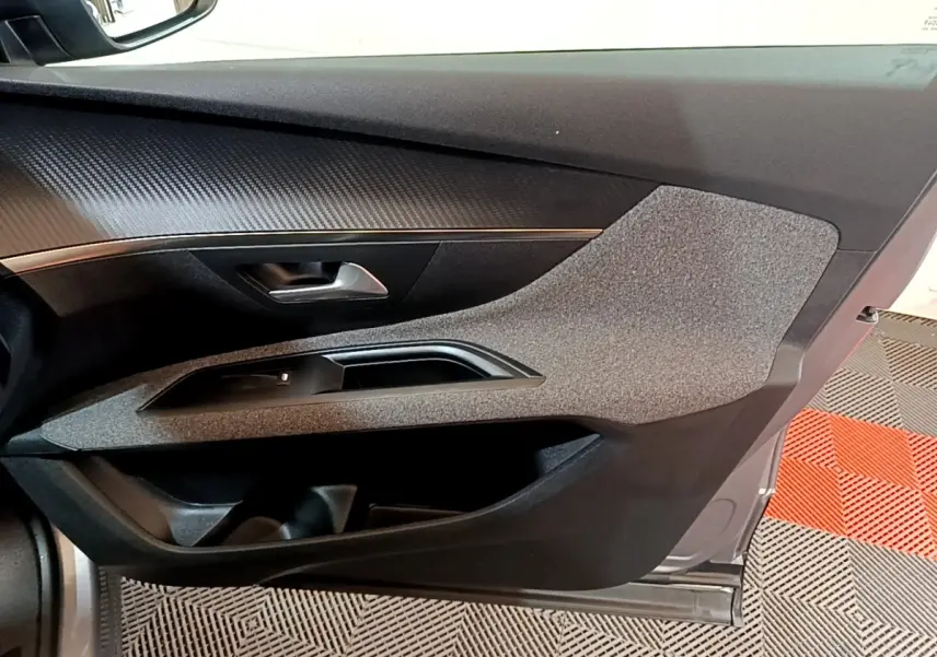Vue intérieure côté gauche de la porte avant d’un Peugeot 5008 gris foncé, avec habillage tissu et plastique noir.