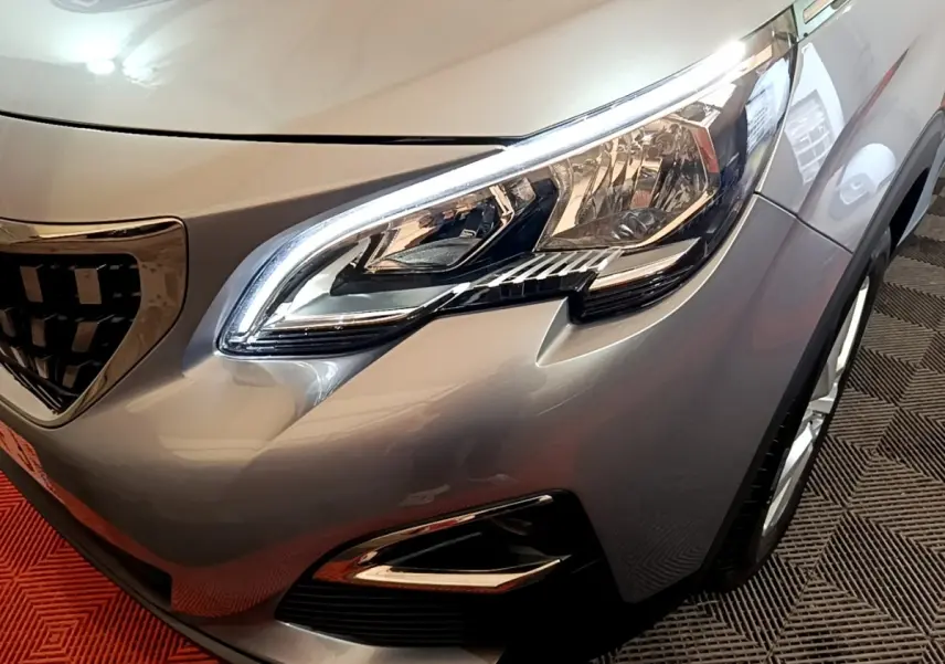 Gros plan sur le phare avant droit du Peugeot 5008 gris foncé, mettant en valeur la calandre et les détails lumineux LED.