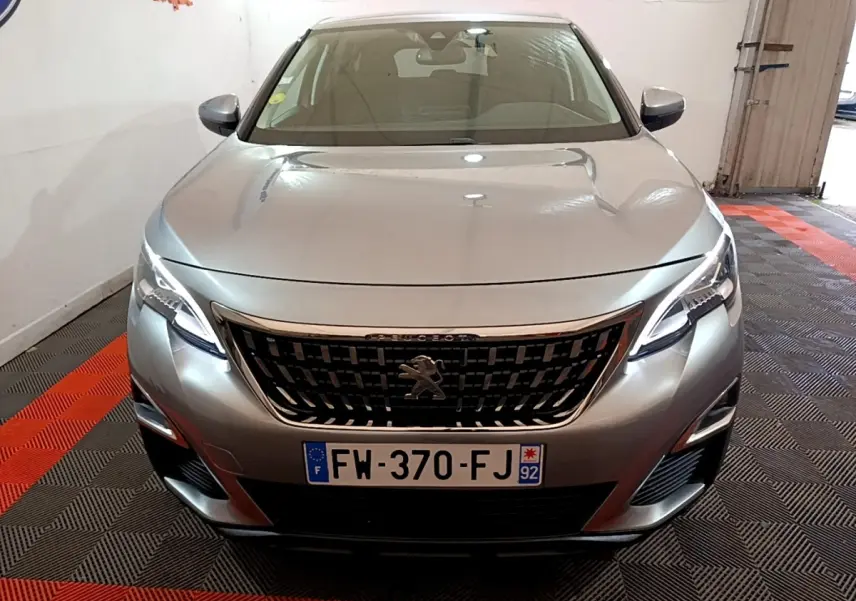 Vue avant frontale d'un Peugeot 5008 gris foncé avec calandre noire et phares LED allumés dans un garage.