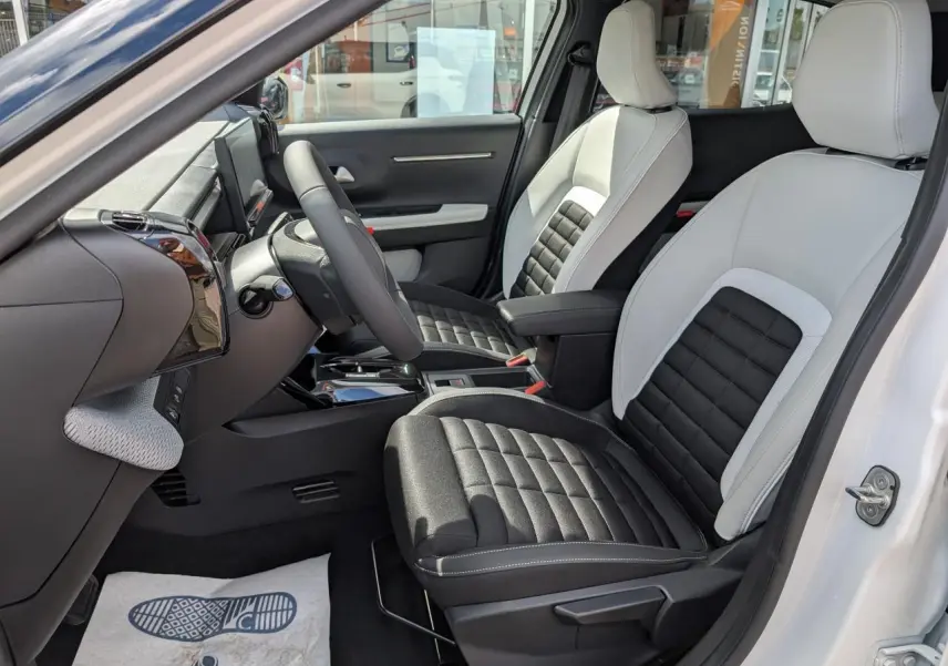 Vue intérieure côté conducteur du Citroën C3 Aircross blanc, sièges bicolores noir et gris avec console centrale et volant multifonctions.