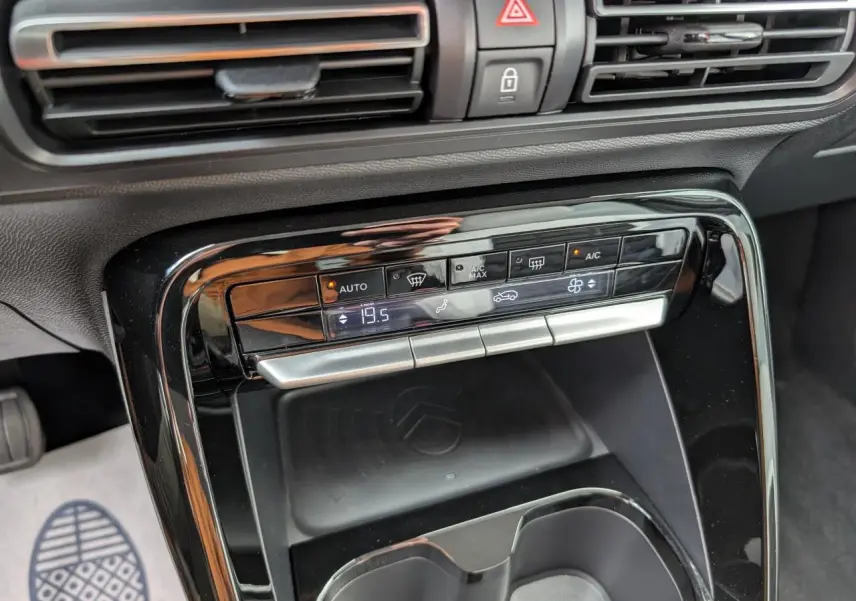 Détail de la console centrale noire brillante avec commandes climatisation et espace de recharge sans fil dans une Citroën C3 Aircross blanche.