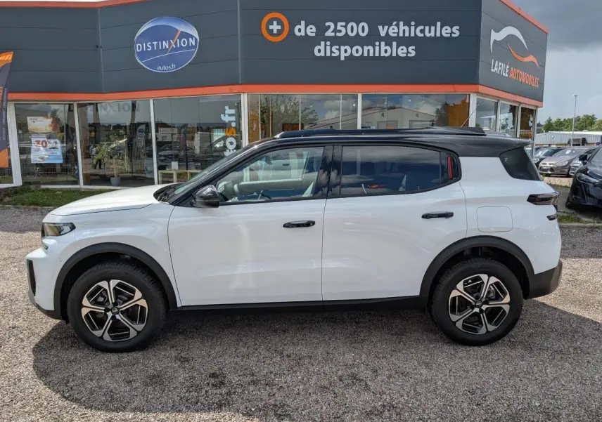 Vue de profil côté gauche du Citroën C3 Aircross blanc avec toit noir et jantes alliage 17 pouces devant un concessionnaire.