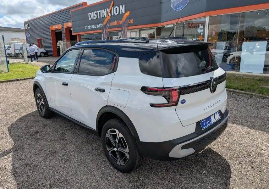Vue 3/4 arrière droite du Citroën C3 Aircross blanc avec toit noir et jantes alliage 17 pouces, stationné devant un garage.