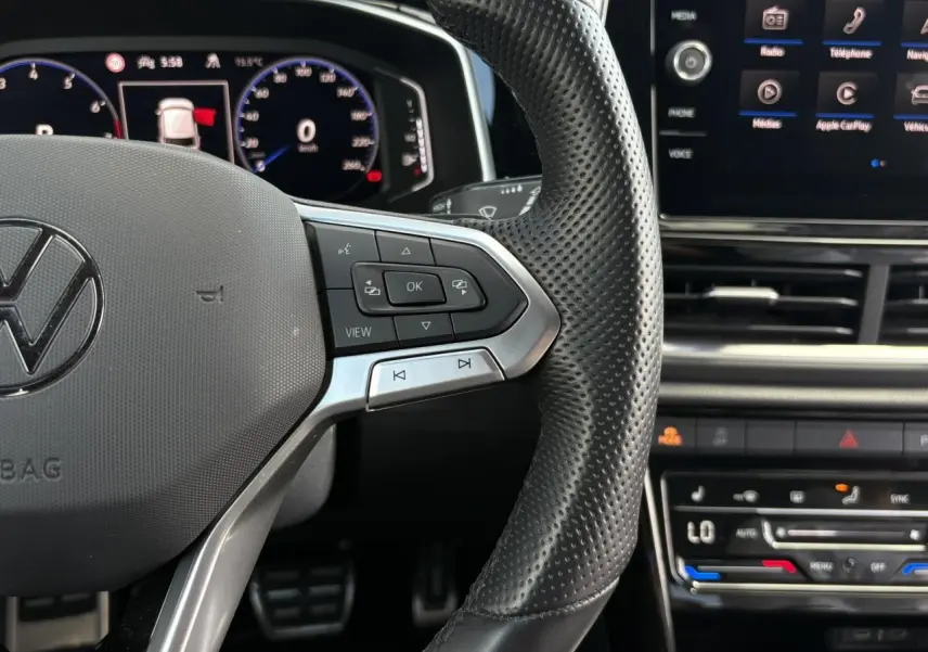 Gros plan sur le volant cuir perforé du Volkswagen T-Roc 2025 avec commandes multifonctions et tableau de bord digital.