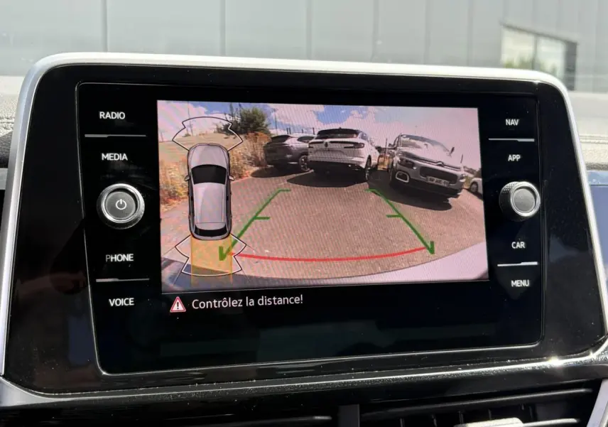 Écran tactile intérieur montrant la caméra de recul du Volkswagen T-Roc gris Indium avec lignes de guidage vertes et rouges.