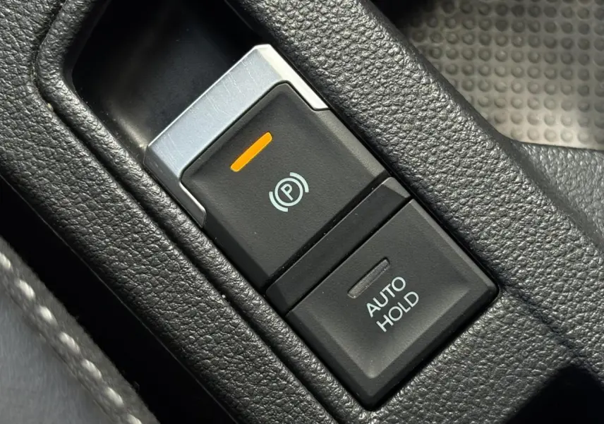 Gros plan sur la commande de frein de stationnement électrique et Auto Hold dans l’habitacle du Volkswagen T-Roc gris Indium.
