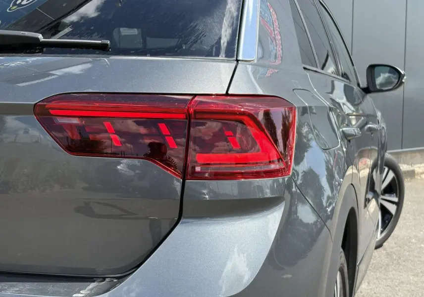 Vue arrière droite du Volkswagen T-Roc gris Indium avec feux arrière LED distinctifs et hayon électrique visible.