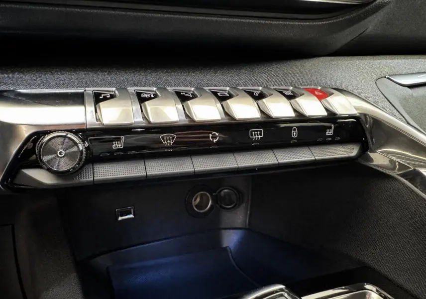 Gros plan sur la rangée de commandes centrales chromées et noires du tableau de bord du Peugeot 5008 noir, version Allure Pack.