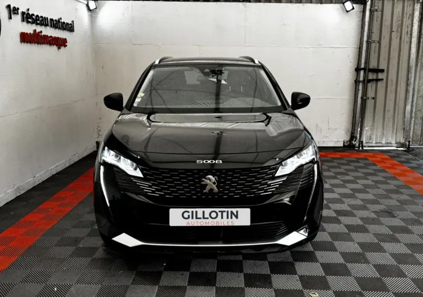 Vue avant d'un Peugeot 5008 noir 2022 avec calandre distinctive et phares LED allumés dans un garage.