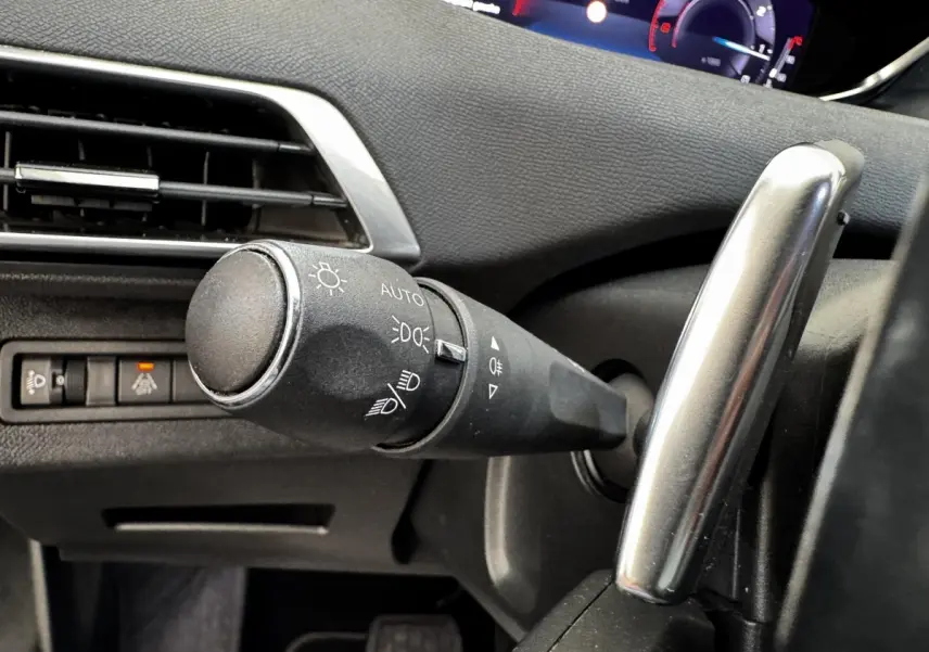 Gros plan sur la commande des phares et clignotants à gauche du volant dans l’habitacle noir du Peugeot 5008 2022.