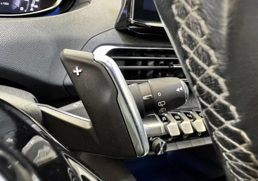 Gros plan sur la palette de changement de vitesse droite en plastique noir et chrome dans l’habitacle du Peugeot 5008 noir.