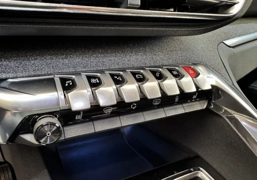 Gros plan sur la rangée de boutons argentés du tableau de bord du Peugeot 5008 noir, avec finition tissu gris.