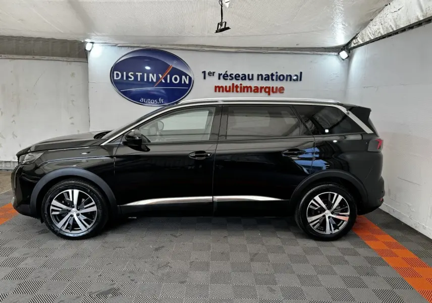 Profil latéral droit d'un Peugeot 5008 noir 2022 avec jantes alliage et barres de toit chromées, en intérieur showroom.
