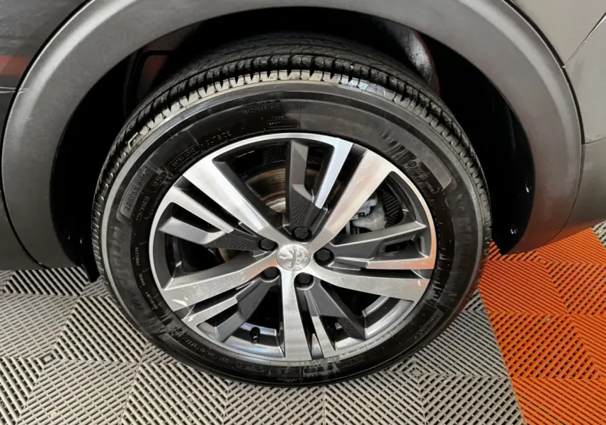 Gros plan sur la roue avant droite du Peugeot 5008 noir, mettant en valeur la jante alliage moderne et le pneu Michelin.