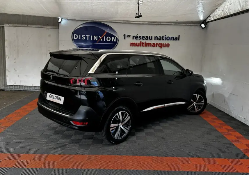 Peugeot 5008 noir vue 3/4 arrière droit dans un garage avec bandeaux chromés et jantes alliage visibles.