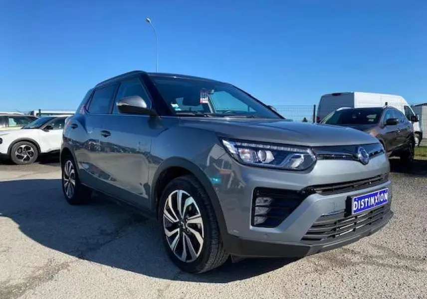 Ssangyong Tivoli gris foncé en vue 3/4 avant droit, avec jantes alliage et calandre moderne sous un ciel bleu.