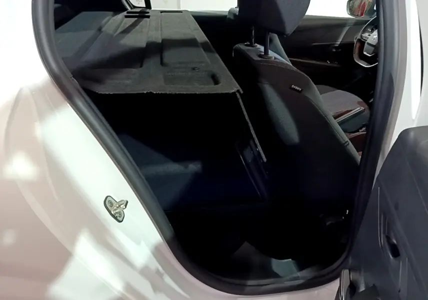 Vue intérieure depuis la porte arrière gauche d’une Peugeot 208 blanche, montrant le coffre avec tablette arrière relevée et siège avant noir.