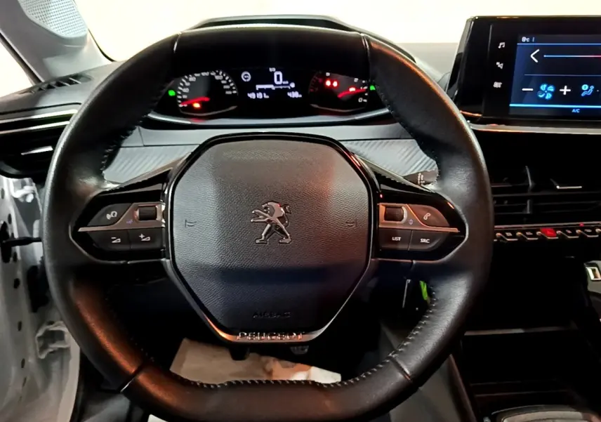 Vue rapprochée du volant noir de la Peugeot 208 1.5 BlueHDi 100 S&S Premium avec tableau de bord et écran tactile visibles.