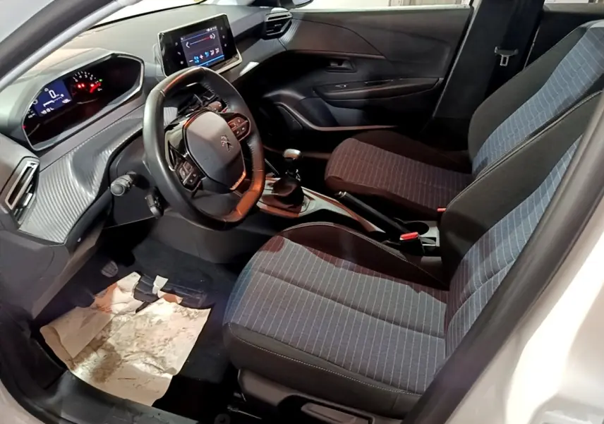 Vue intérieure côté conducteur de la Peugeot 208 1.5 BlueHDi 100 S&S Premium, montrant sièges tissu gris et tableau de bord moderne.
