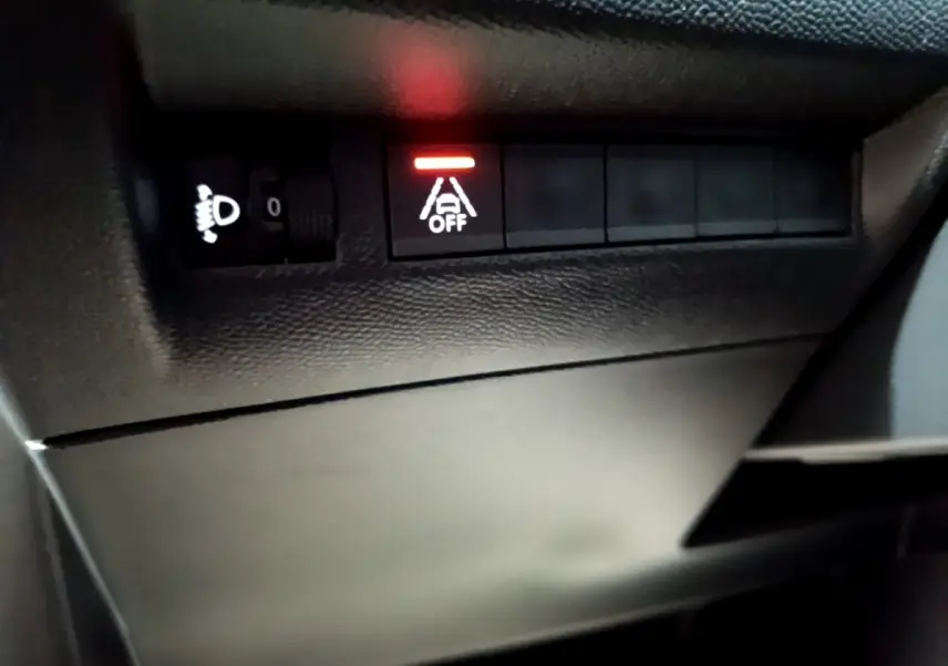 Gros plan sur les commandes noires du tableau de bord côté gauche du Peugeot 208 blanc, voyant d'alerte allumé rouge.