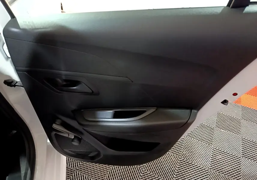 Vue rapprochée de la porte arrière gauche noire intérieure d’une Peugeot 208 blanche, avec poignée et commande manuelle de vitre.
