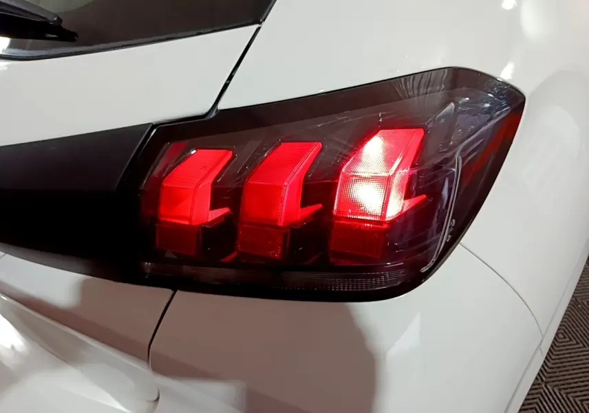 Gros plan sur le feu arrière droit rouge d’une Peugeot 208 blanche, soulignant le design en trois griffes distinctives.