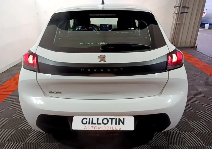 Vue arrière d'une Peugeot 208 blanche de 2021 avec feux LED allumés et logo lion central sur bande noire.