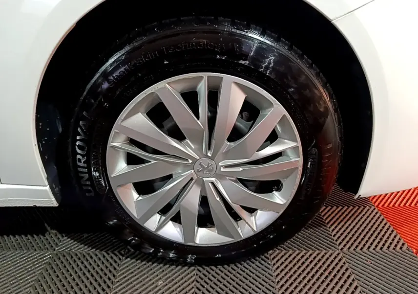 Gros plan sur la roue avant droite d'une Peugeot 208 blanche, mettant en valeur la jante alu au design moderne.