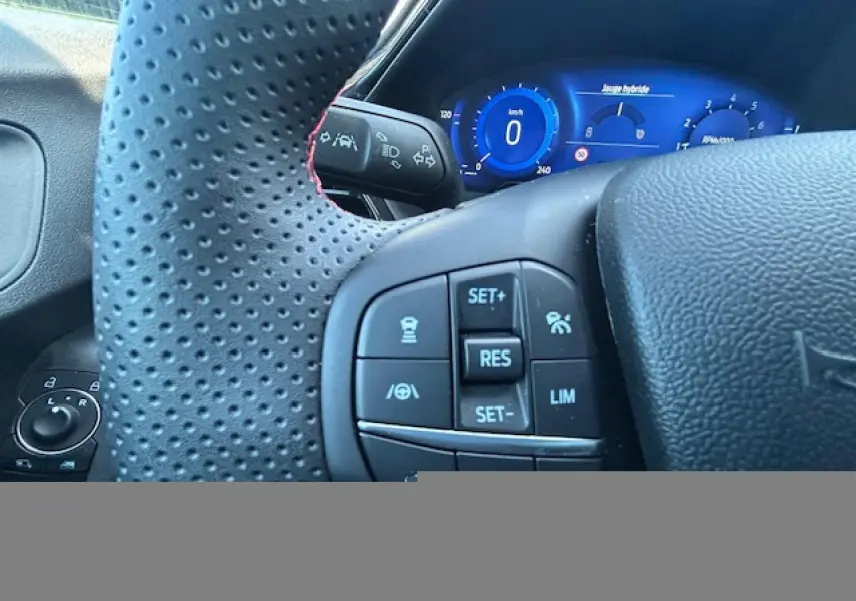 Gros plan sur le volant perforé avec surpiqûres rouges et le combiné numérique bleu du Ford Puma II gris Magnetic, version ST-Line.