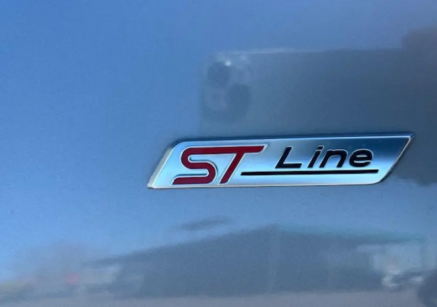 Gros plan sur le badge ST-Line rouge et noir sur la carrosserie gris magnetic d'un Ford Puma 2023.