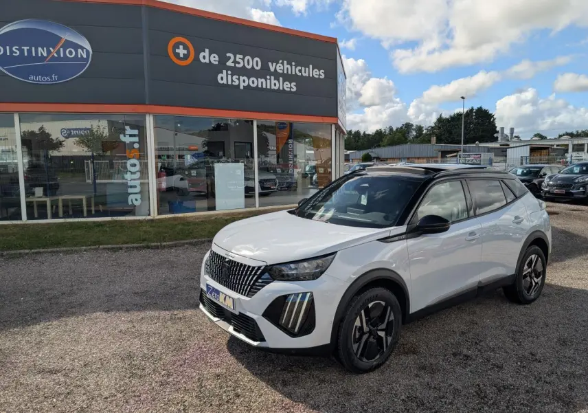 Peugeot 2008 blanc vue 3/4 avant droit avec toit noir et jantes alliage bi-ton devant un concessionnaire.