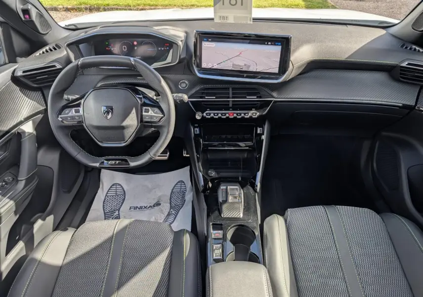 Vue intérieure avant du Peugeot 2008 GT hybride 2026, avec volant compact, écran tactile 10 pouces et sellerie tissu noire à surpiqûres vertes.