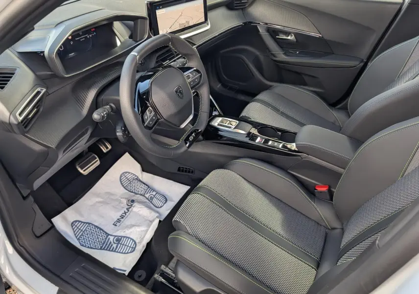 Vue intérieure côté conducteur du Peugeot 2008 GT 2026, sièges tissu gris avec surpiqûres vertes et volant compact cuir noir.
