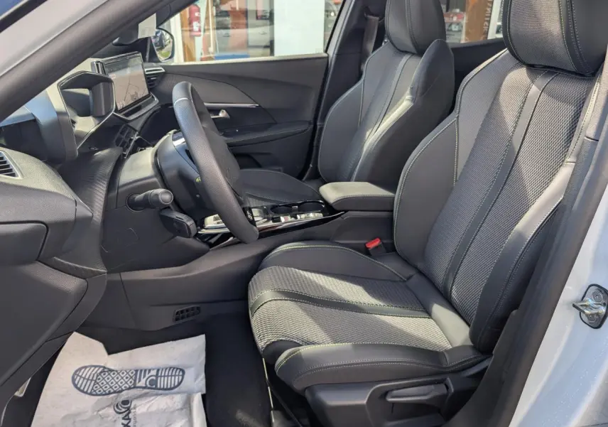 Vue intérieure côté conducteur du Peugeot 2008 blanc 2026, sièges sport gris avec surpiqûres vertes et tableau de bord moderne.